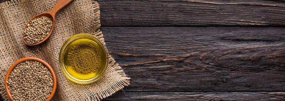 Hemp oil and hemp seeds in bowls over wooden background, top view.