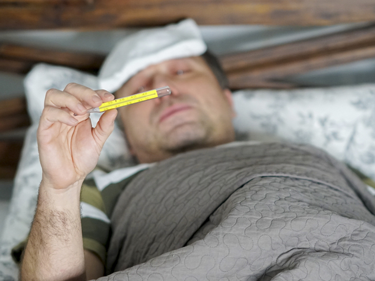Sick and tired man lying in bed checking his temperature